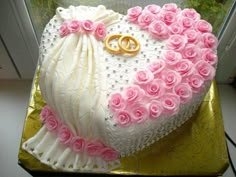 a heart shaped cake decorated with pink roses and two gold wedding rings