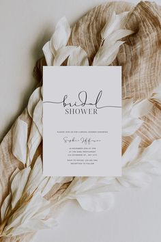 a white card with black ink that says bridal shower on it, surrounded by feathers