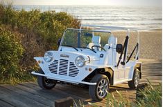 a white jeep parked on top of a wooden platform next to the ocean and grass