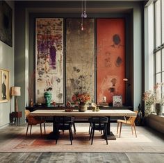 a dining room table with chairs and paintings on the wall behind it in front of large windows