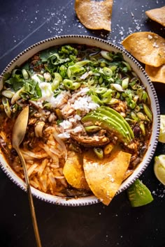 a bowl filled with tortilla soup and topped with avocado, sour cream, cilantro, green beans, shredded cheese and sliced lime wedges