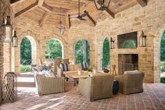 an outdoor living room with stone walls and brick flooring is furnished with wicker furniture