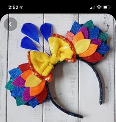 a colorful mickey mouse ears headband with sequins and feathers on it's side