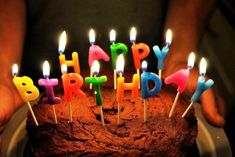 a person holding a cake with lit candles on it in front of the words happy birthday