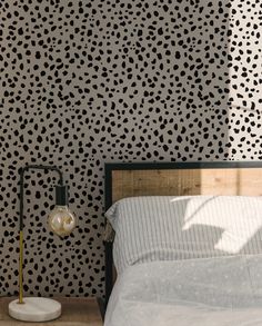 a bed sitting next to a lamp on top of a wooden table in front of a black and white wall