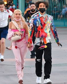 a man and woman walking down the street wearing face masks, with other people behind them