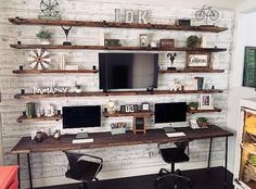 a computer desk with two monitors on it in front of a wall mounted tv and shelves