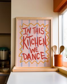 this kitchen we dance sign is on the counter next to a potted plant and utensils