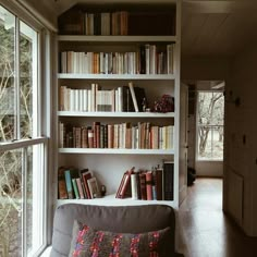 a living room filled with lots of books on top of a white book shelf next to a window