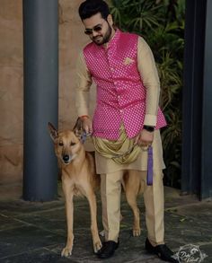 a man in a pink shirt and tan pants standing next to a dog