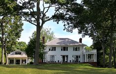 a large white house sitting in the middle of a lush green field next to trees