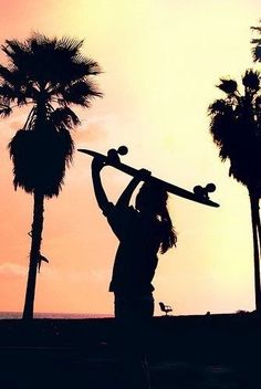 a person holding a skateboard up to their head in the air with palm trees behind them