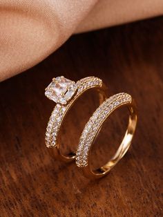 two gold wedding rings with diamonds on top of each other, sitting on a wooden surface