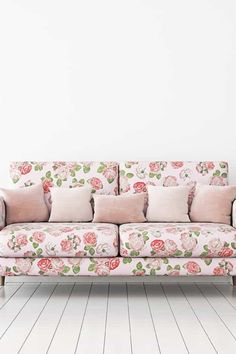 a pink floral couch sitting on top of a hard wood floor next to a white wall