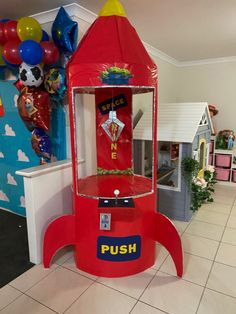 a small red toy rocket ship on display in a children's playroom with balloons