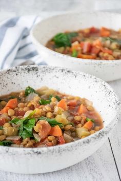 two white bowls filled with vegetable soup on top of a wooden table next to a blue and white towel