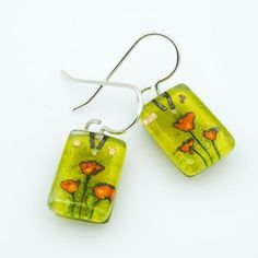 Golden Poppies is part of the VERDANT collection. Where Edo grew up in Northern California, the roadsides are often replete with these brilliantly colored flowers. All children in California are taught, growing up, that the golden poppy is the state flower and it is illegal to pick it -- a very early lesson in civics.All of our dangle earrings are finished with premium Argentium silver wires and include a pair of silicone ear backs. Argentium silver is a step up from sterling silver; it is 100% Hand Painted Green Flower Earrings, Green Hand Painted Flower Earrings, Green Drop Earrings With Birth Flower, Green Birth Flower Drop Earrings, Artistic Green Flower-shaped Jewelry, Golden Poppies, Golden Poppy, Fused Glass Earrings, Fused Glass Artwork