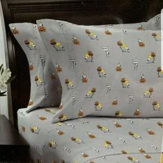 a bed with gray sheets and yellow flowers on it, next to a night stand