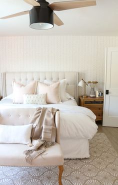 a bedroom with a white bed, beige pillows and a ceiling fan in the corner