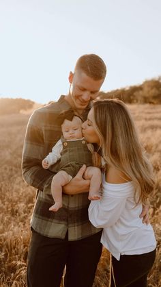 a man and woman holding a baby in their arms while standing in the middle of a field