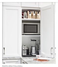 a kitchen with white cabinets and an open microwave above the counter top is full of coffee