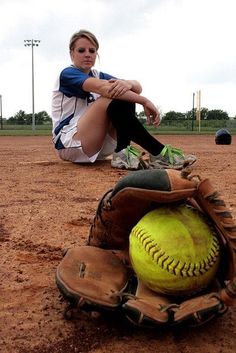 a woman sitting on top of a baseball field next to a yellow ball and glove