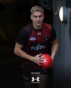 a young man holding a red ball in his right hand and looking at the camera