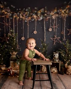 a baby standing on a stool in front of christmas decorations and garlands, smiling at the camera