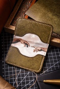 a wallet with the creation of adam on it sitting next to some scissors and thread