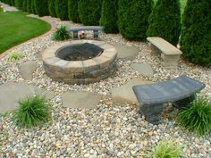 an outdoor fire pit surrounded by rocks and gravel with benches around it in the middle