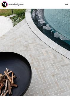 a black bowl with wood in it on the ground next to a swimming pool and firewood