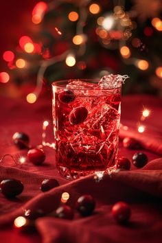 a glass filled with red liquid next to a christmas tree covered in lights and ornaments