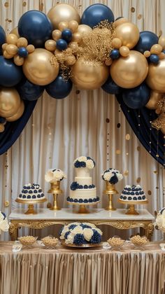 a table topped with blue and gold desserts next to a balloon filled wall in the background