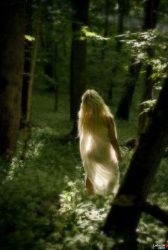 a woman is walking through the woods with long hair on her head and in white dress