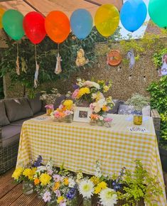 a table covered with flowers and balloons in the middle of an outdoor patio area that is decorated for a birthday party