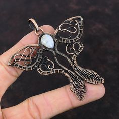 a hand holding a silver pendant with a white stone in the shape of a butterfly