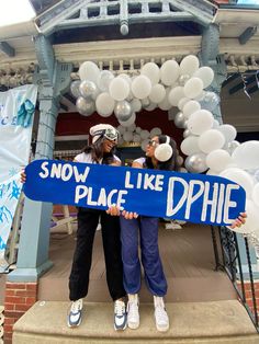 two women holding a snow like sign and balloons