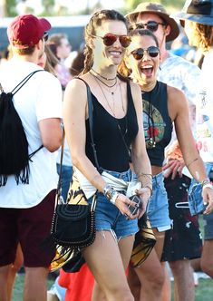 two young women are laughing while walking through the crowd at an outdoor music festival together