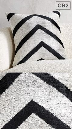 a black and white pillow sitting on top of a couch next to a blanket with the word cb2 printed on it