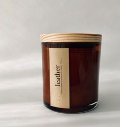 a candle with a label on it sitting in front of a white background that says letter