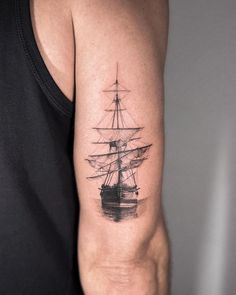 a black and white photo of a ship tattoo on the left upper half of the arm