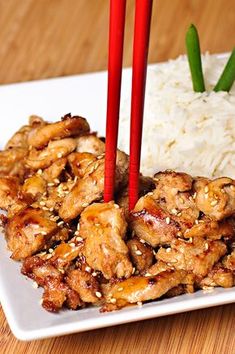 a white plate topped with chicken and rice next to chopsticks on a table