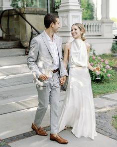 a bride and groom walking down the sidewalk holding hands in front of a white building