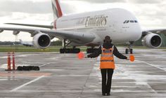 a woman in an orange vest is walking towards a large airplane on the tarmac