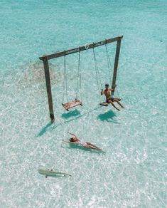 two people are in the water on swings and one person is lying on a surfboard