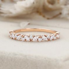 a rose gold wedding band with five diamonds on it and white flowers in the background