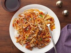 a white plate topped with pasta and sauce next to a glass of wine on top of a wooden table