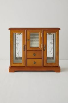 a small wooden cabinet with glass doors and drawers on the bottom shelf, against a white background