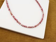 This Burma Jade Choker Necklace is a stunning handmade piece that beautifully showcases the natural charm of rhodonite gemstones. Known for its soft pink marbling, each bead is unique, reflecting the stone's natural beauty and character.  The delicate choker design sits gracefully around the neck, offering a lightweight and comfortable fit for everyday wear. Its minimalist aesthetic enhances both casual and formal outfits, while the natural beauty of the natural Rhodonite gemstones adds a timeless, elegant appeal.  Ideal for women who appreciate elegant yet soulful jewelry. The rhodonite is often associated with emotional healing and compassion, adding a meaningful touch to your accessory collection. This rhodonite crystal choker is perfect for everyday wear or as a thoughtful gift for a l Jade Choker, Choker Design, Gemstone Choker Necklace, Delicate Choker, Pink Rhodonite, Choker Designs, Gemstone Choker, Stone Choker, Formal Outfits