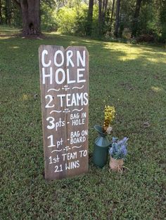 a wooden sign sitting on top of a grass covered field next to flowers and plants